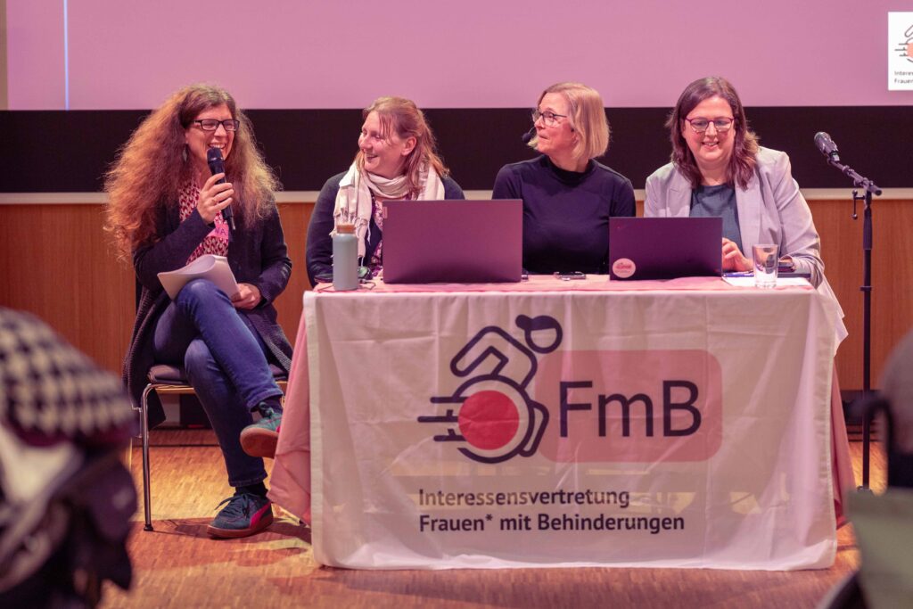 Nina spricht ins Mikrofon. Rechts von ihr sitzen Eva, Julia und Heidemarie. Alle lächeln.