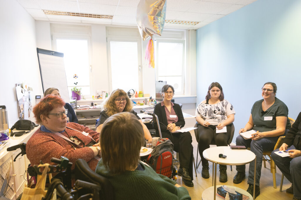 Kleingruppe von 6 Frauen mit Behinderungen in einem kleineren Zimmer - Sesselkreis