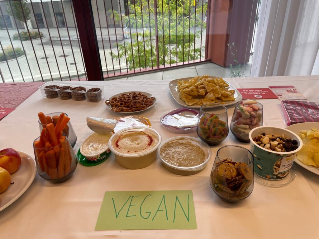 Verschiedene süße und salzige Snacks stehen auf einem Tisch angerichtet, darunter ein Kärtchen mit der Aufschrift "vegan". 
